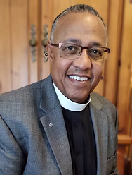 Smiling clergyman in glasses and clerical collar.